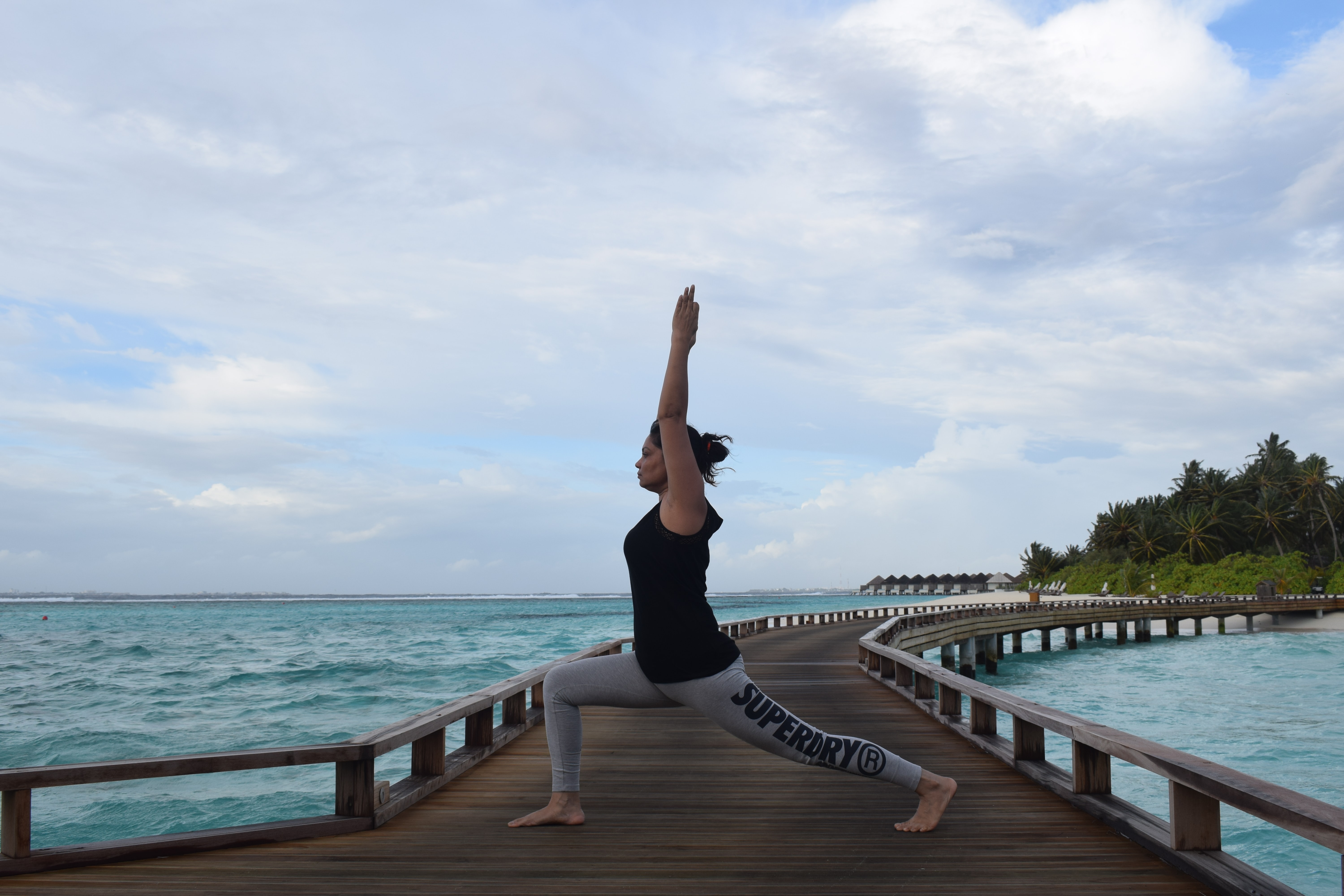 A lady doing Warrior I yoga pose by the ocean.