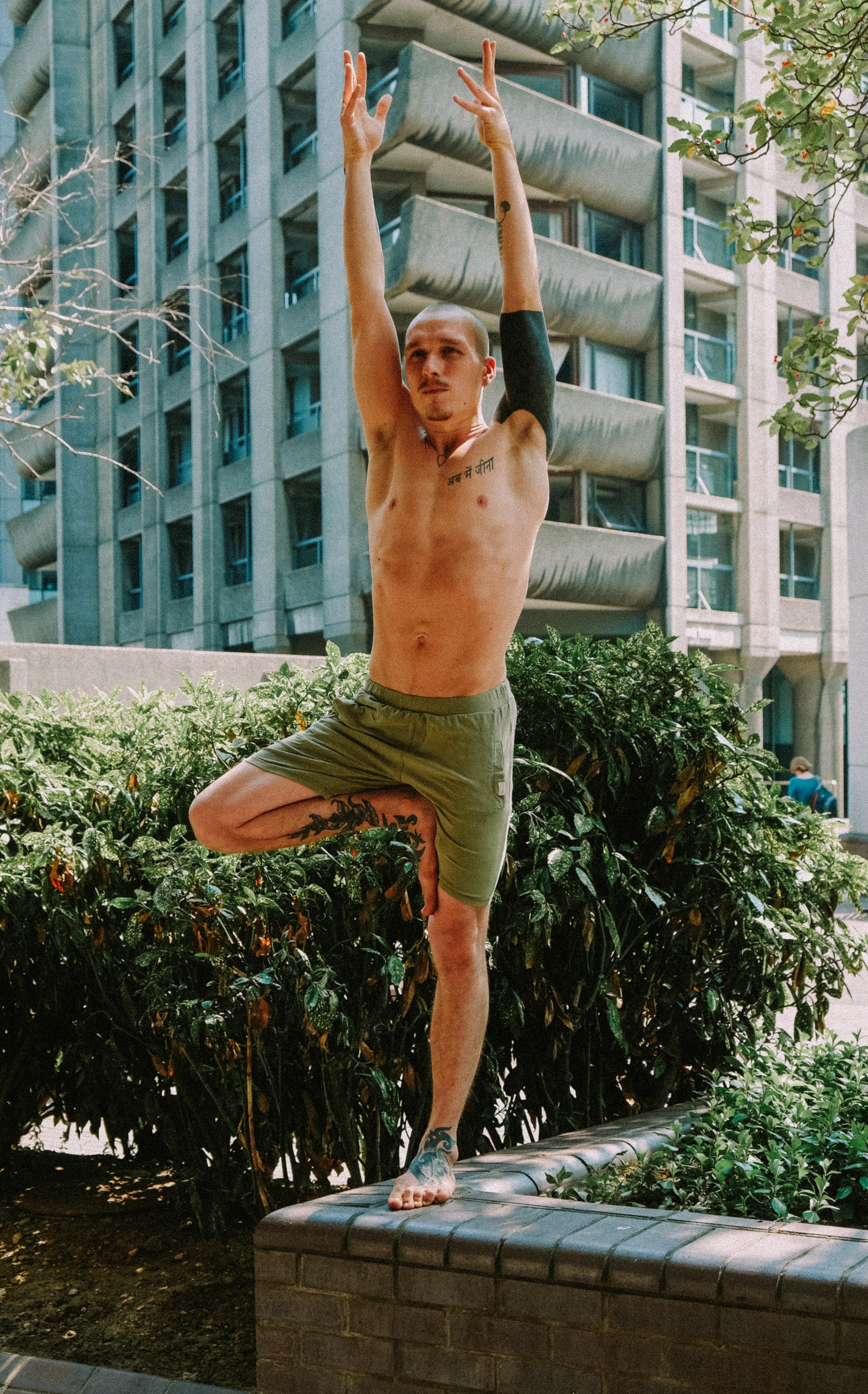 Man doing tree yoga pose by a white building.