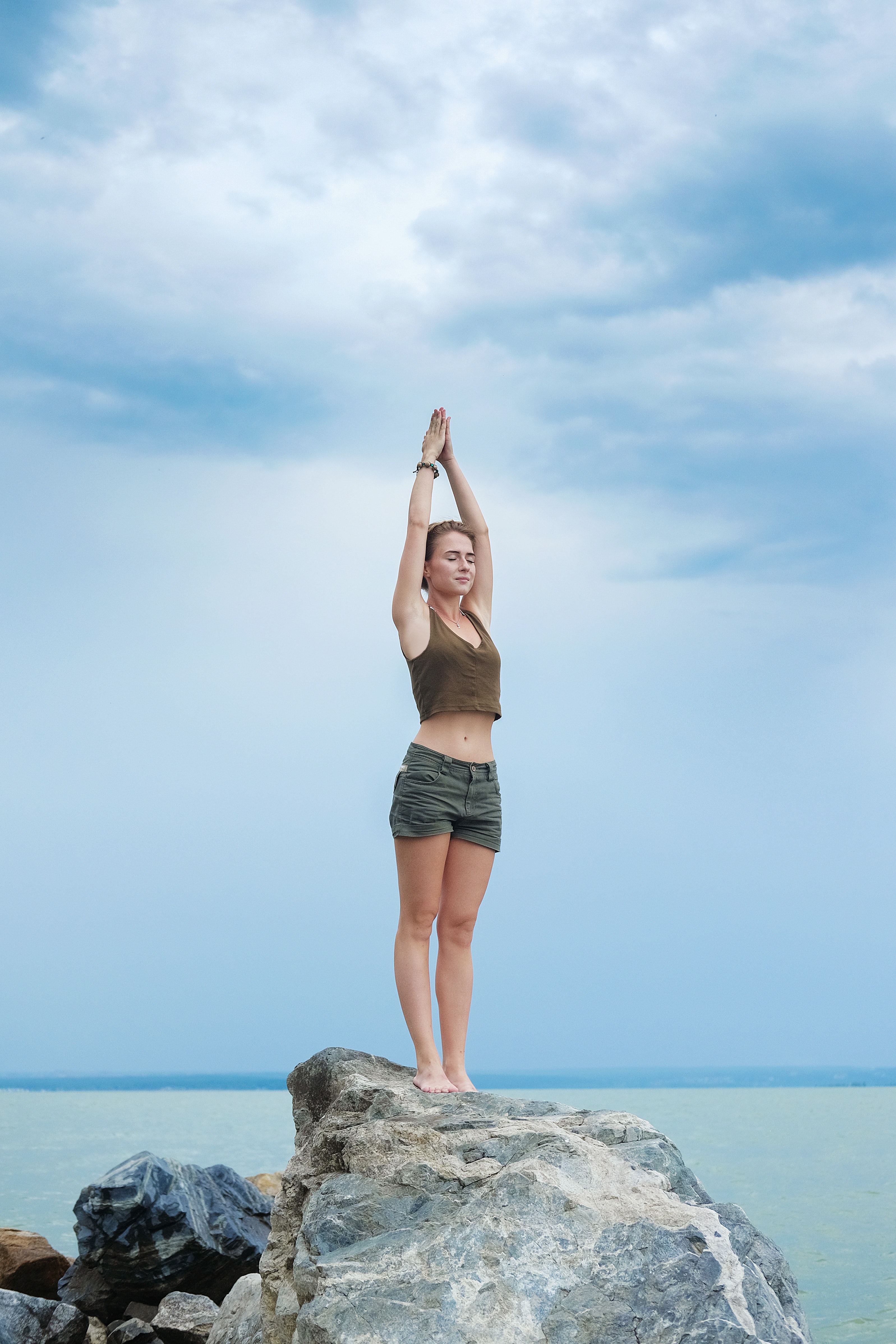 woman doing mountain pose with hands above head on coast of ocean