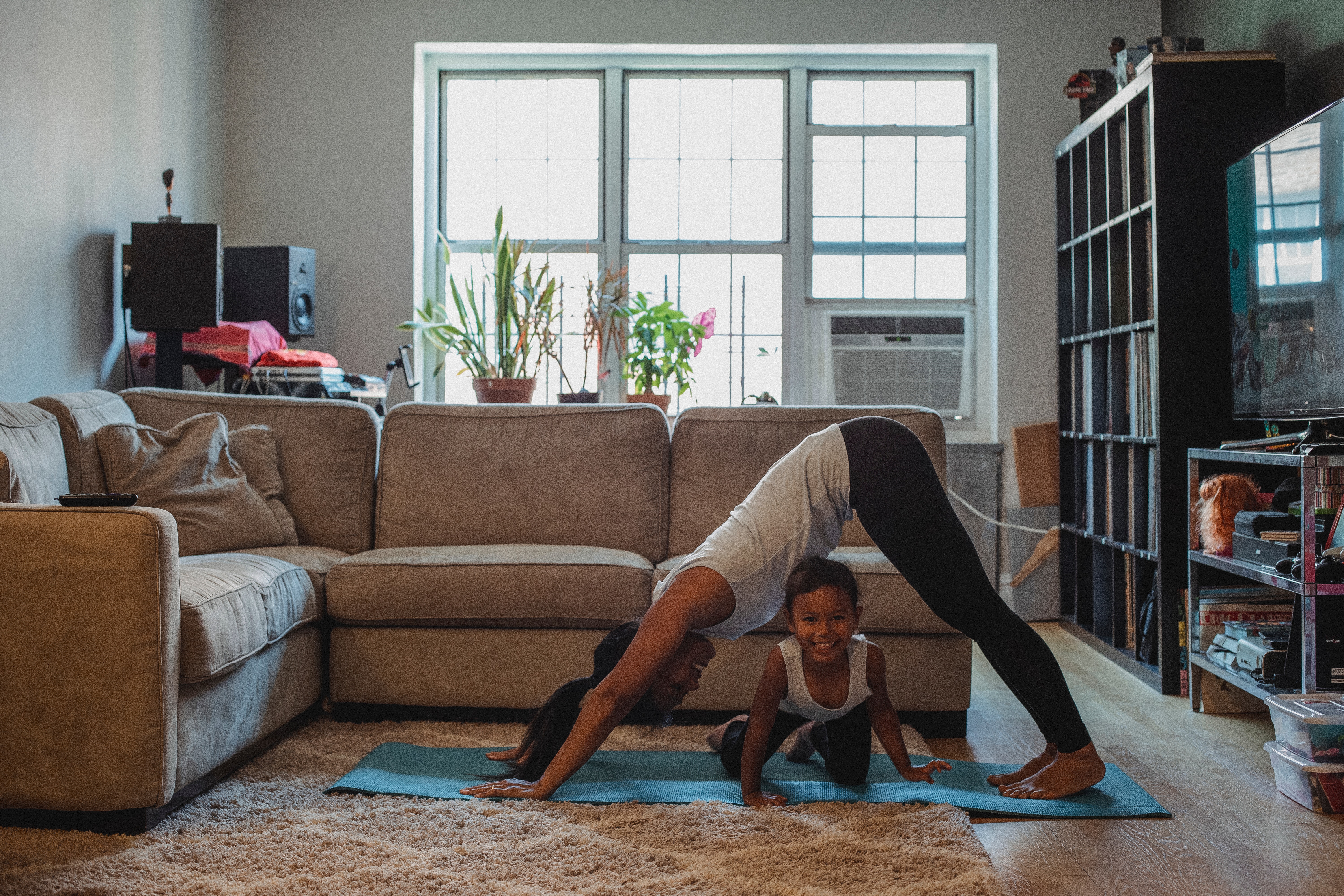 young woman performing warrior pose in living room with daughter nearby